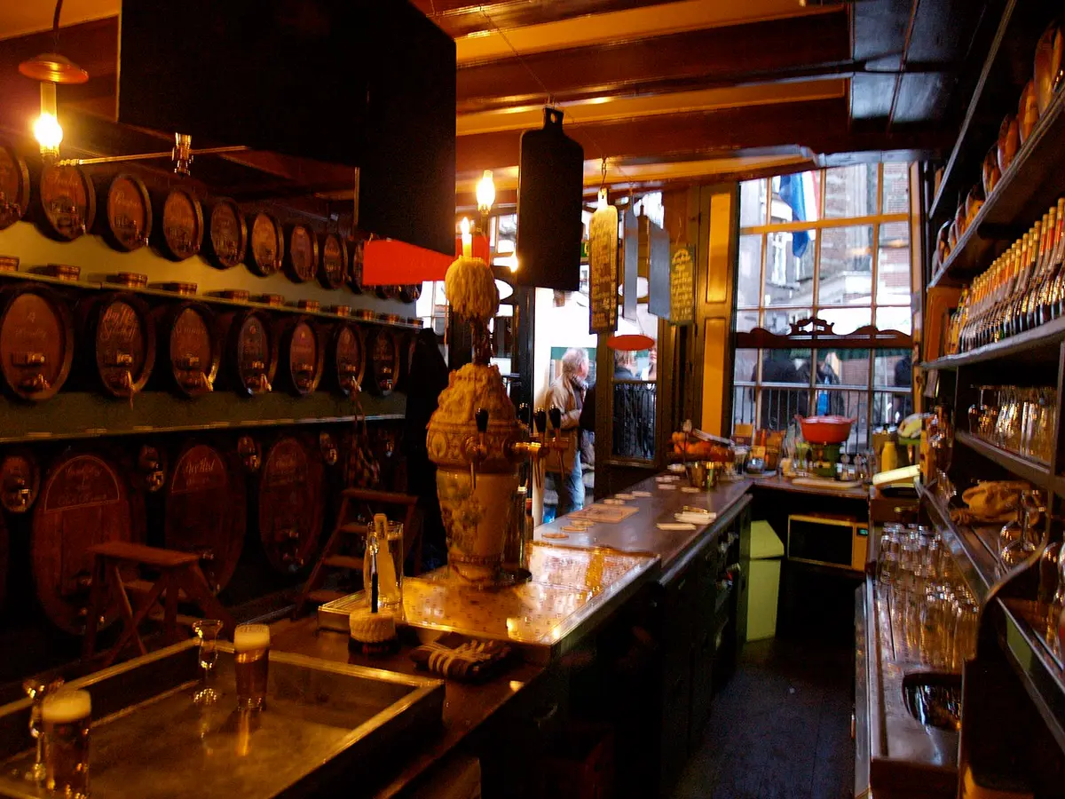 A wooden bar with rows of old casks on the wall behind it, in a jenever tasting room