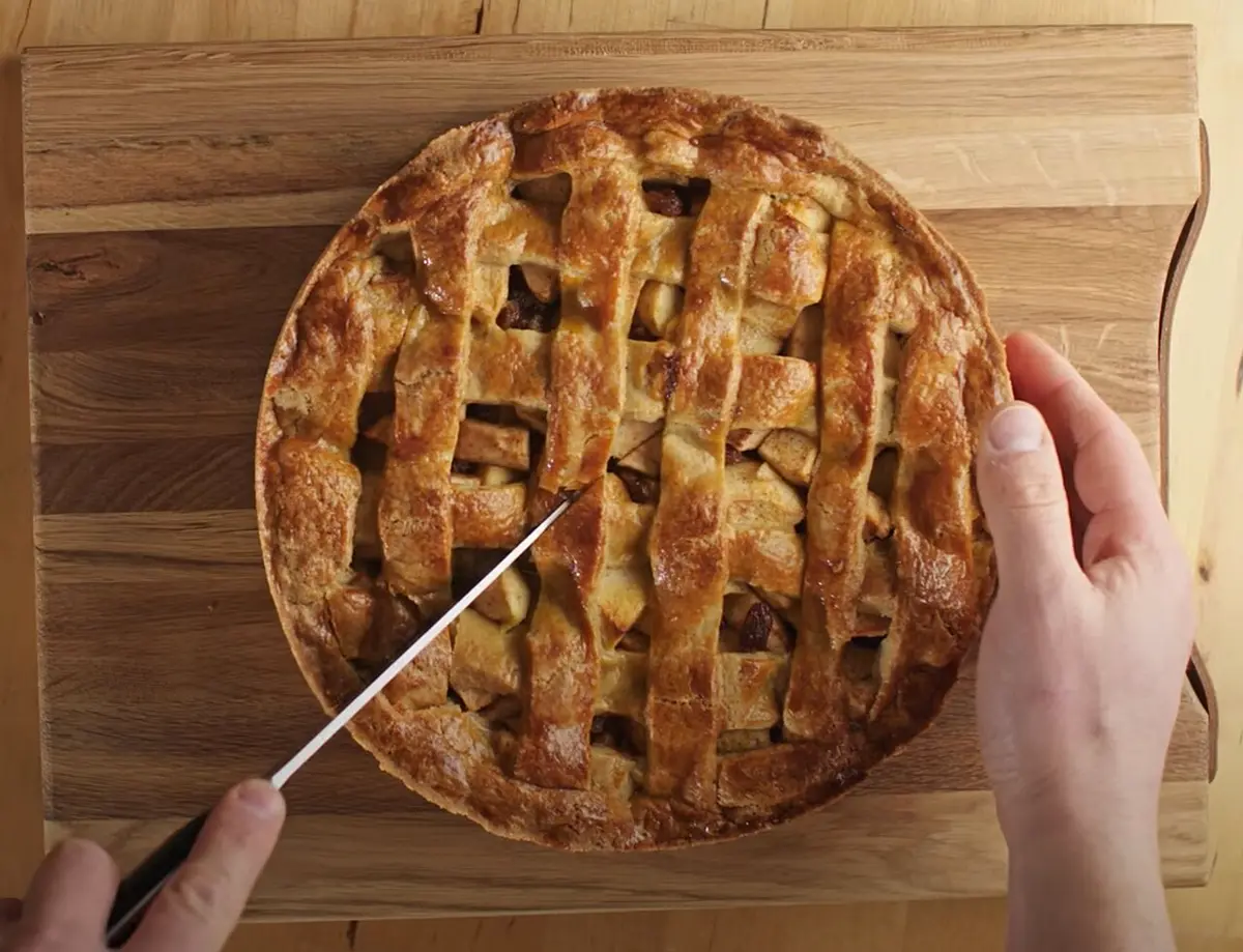 A lattice-topped Dutch apple pie being cut on a wooden board