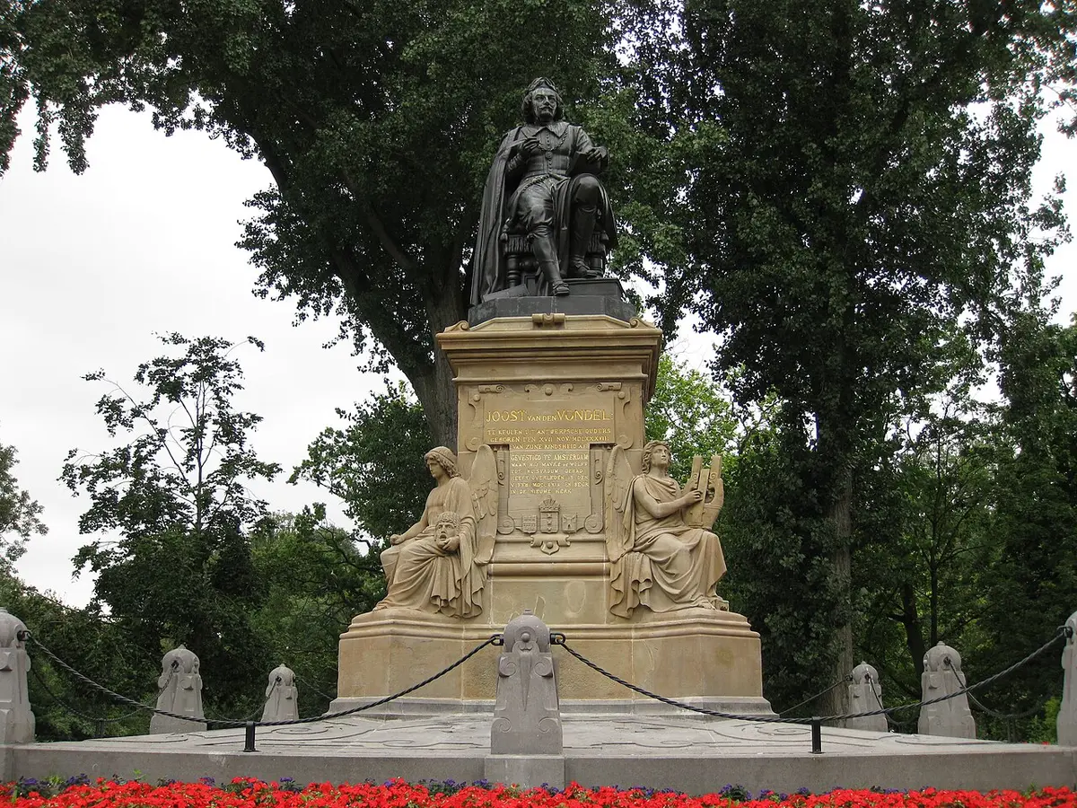 The statue of Vondel seated on a tall stone pedestal among the trees of the Vondelpark