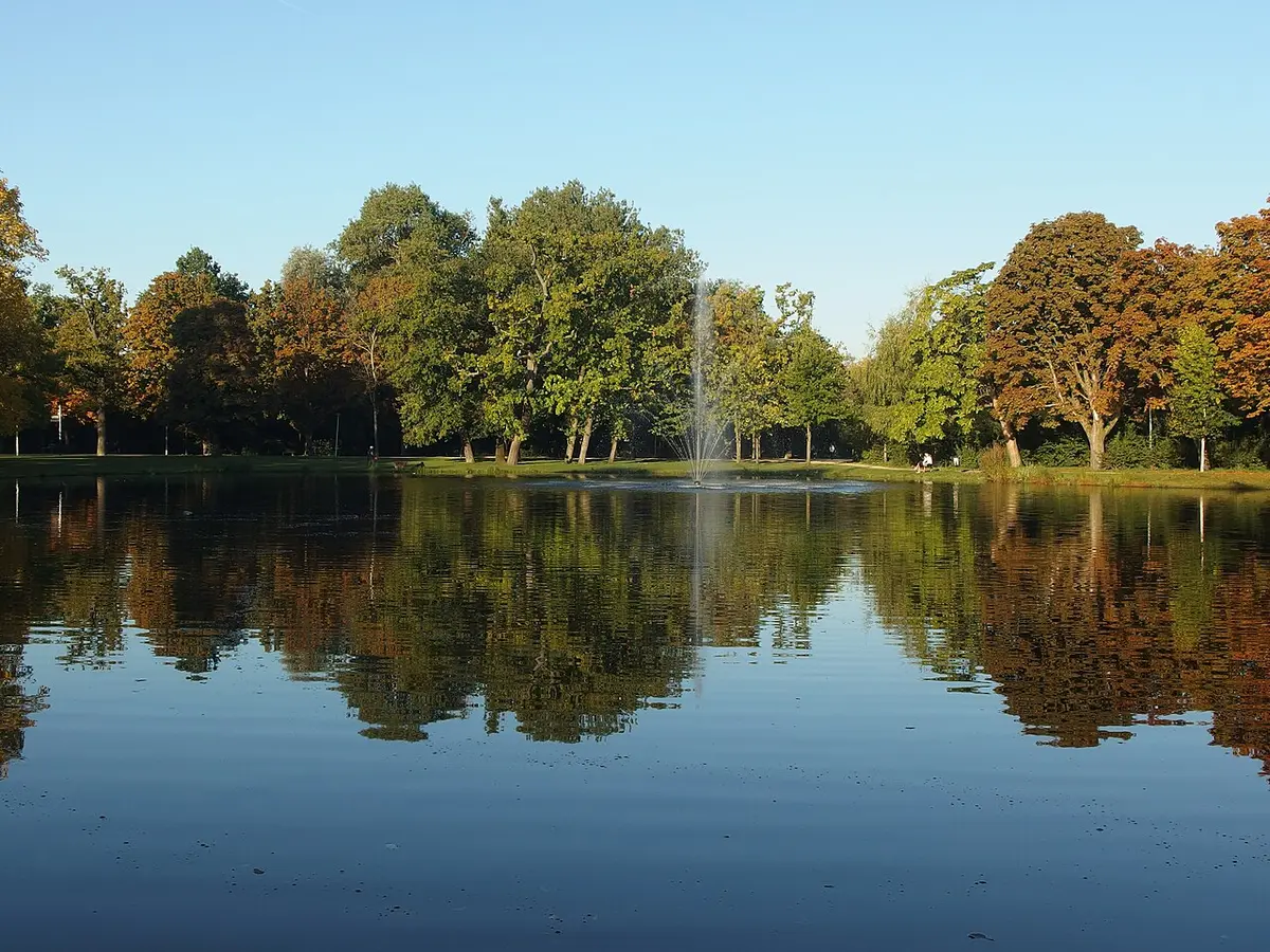 A pond in the Vondelpark with a fountain, autumn trees reflected in the water