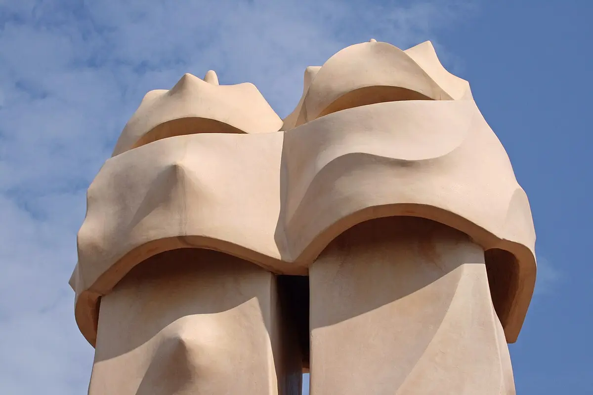 Two cream stone chimneys on the roof of La Pedrera, shaped like helmeted heads, against a blue sky