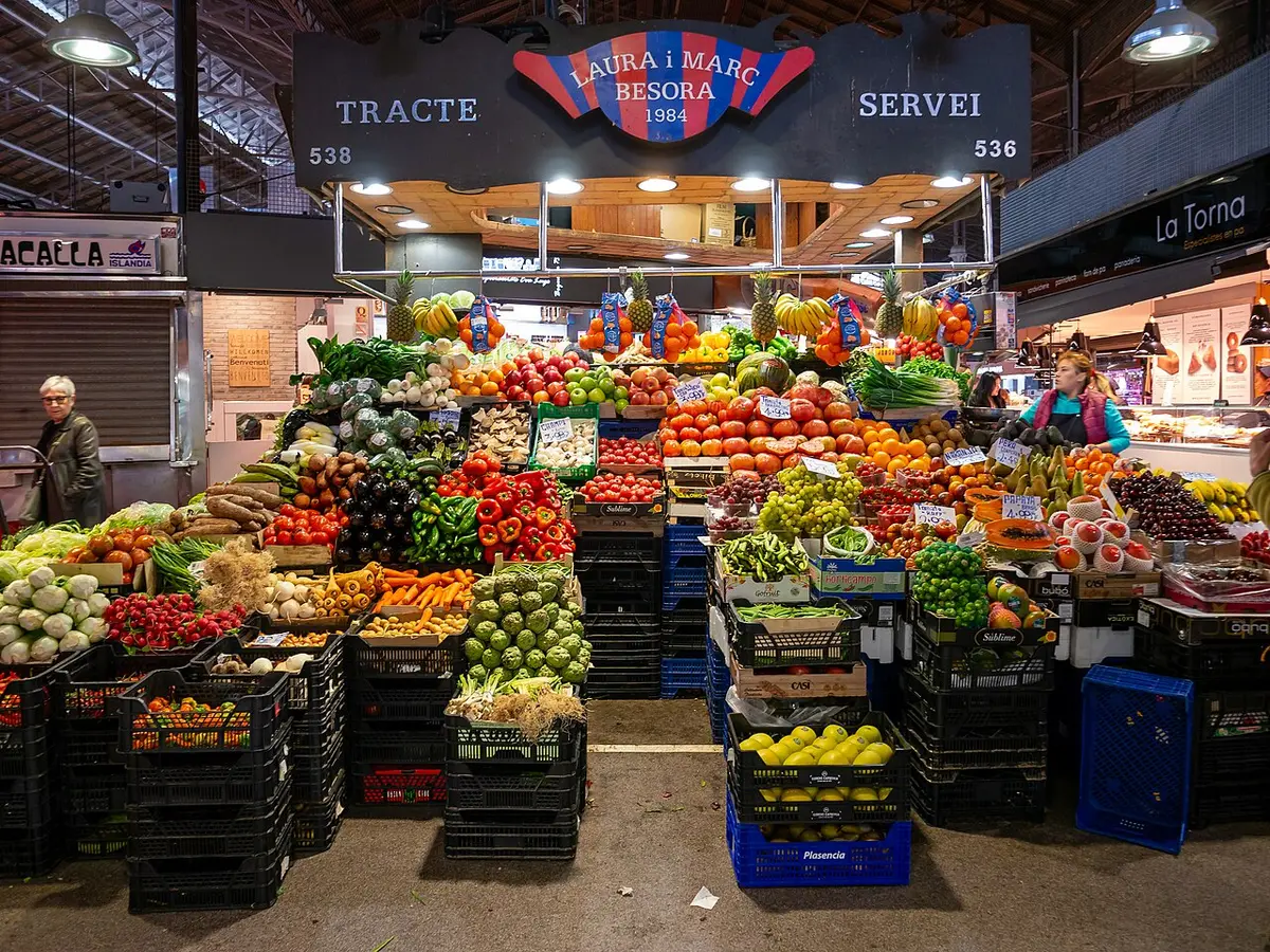 A fruit and vegetable stall piled high under the iron roof of La Boqueria market in Barcelona