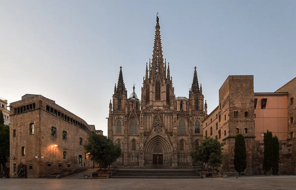 The Gothic facade and spire of Barcelona Cathedral at dusk, with the empty square in front