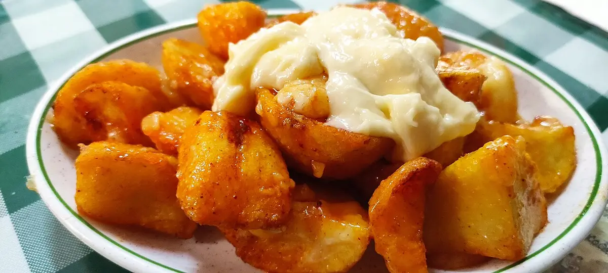 Fried potatoes under a spicy red sauce and white allioli