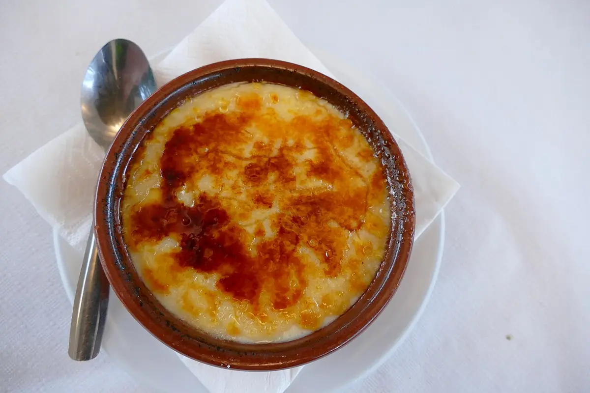 Crema catalana with a burnt sugar crust in a clay dish, a spoon beside it