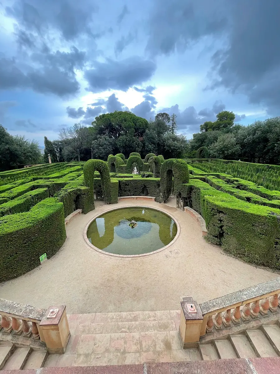 A maze of clipped cypress hedges seen from above, with a round pool at its entrance