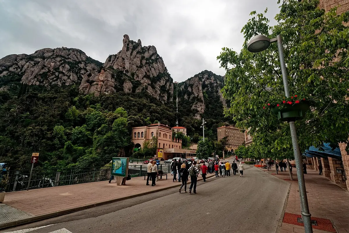 The monastery buildings of Montserrat below jagged rock peaks, with visitors walking along the road