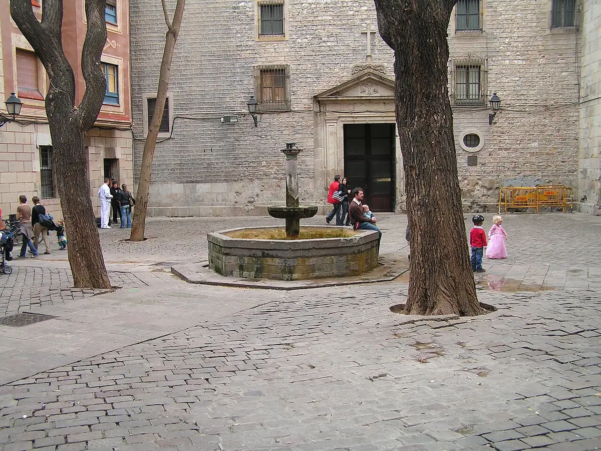 The small Plaça de Sant Felip Neri with its fountain, two trees and the pitted stone front of the church