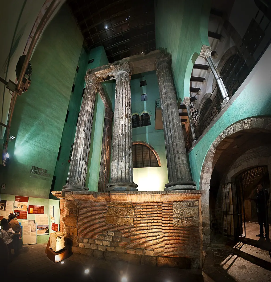 Tall fluted Roman columns with part of their entablature, standing on a stone podium inside a lit courtyard