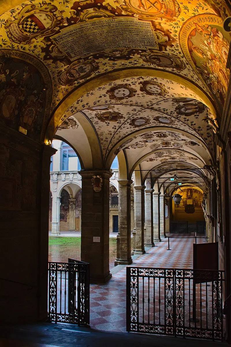 An arcaded loggia of the Archiginnasio, its vaults painted with coats of arms and inscriptions
