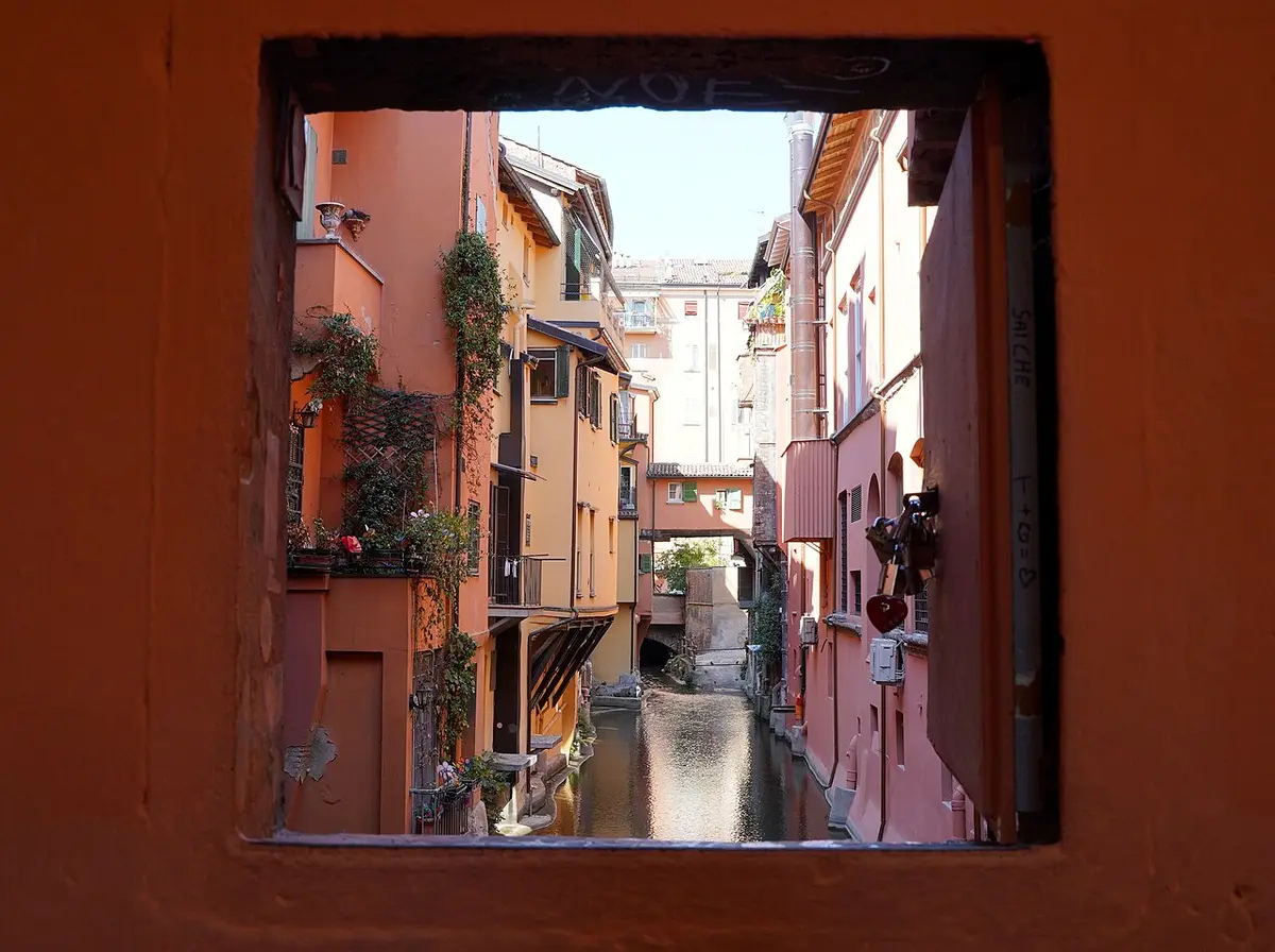 A small window in a red wall opening onto a canal between old houses