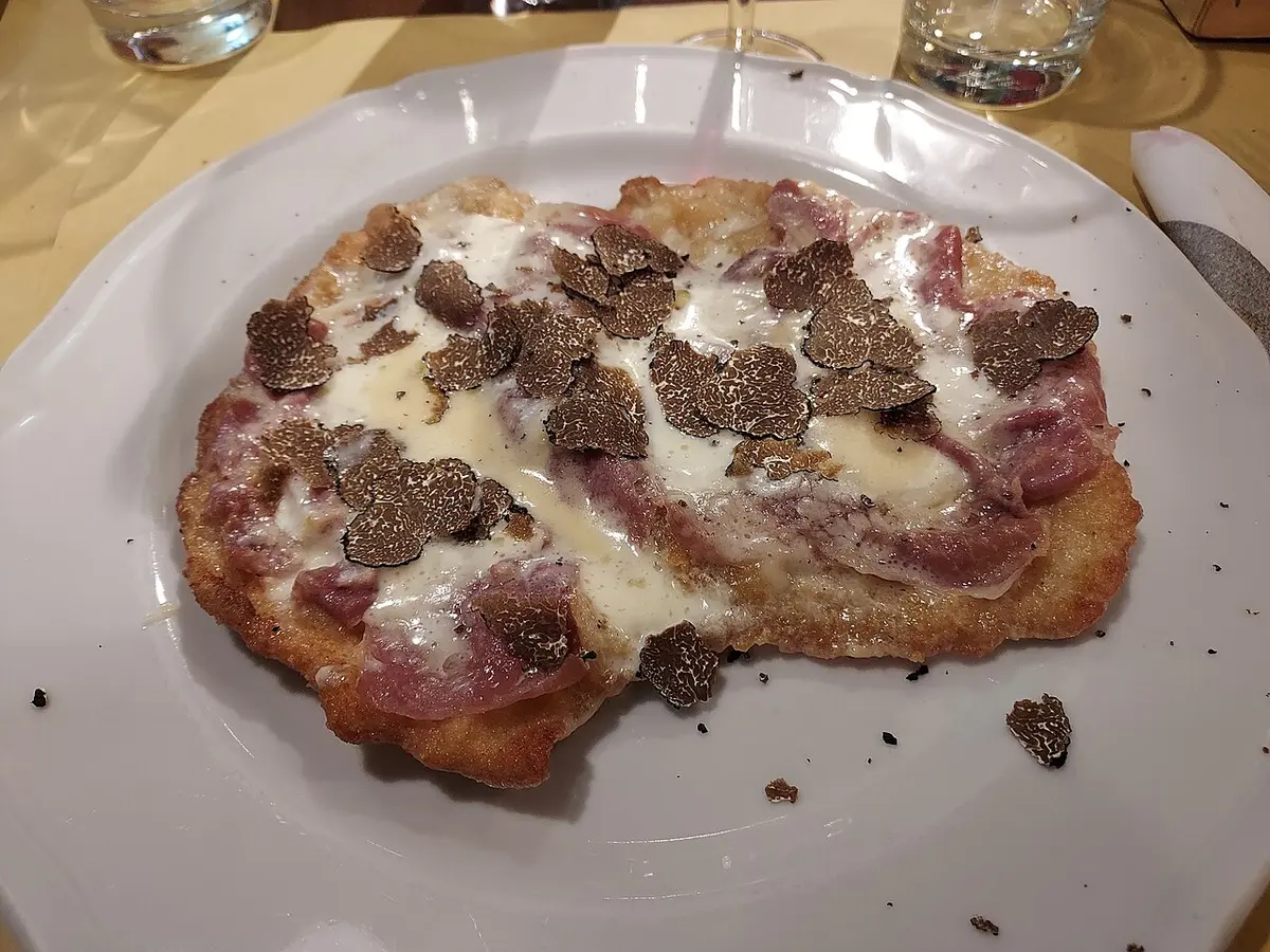 A breaded veal cutlet covered with prosciutto, melted cheese and slices of black truffle