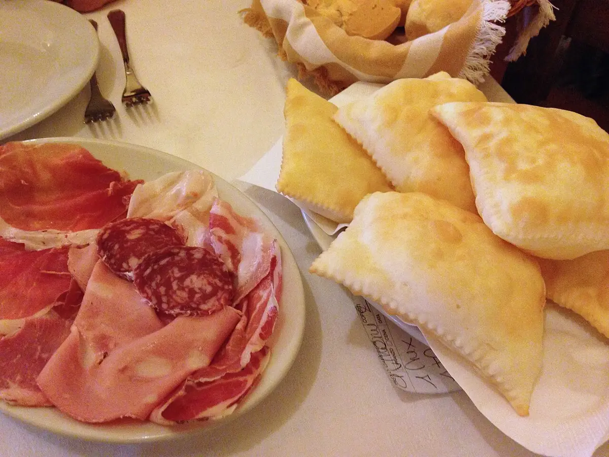 Puffed pillows of fried dough beside a plate of prosciutto, mortadella and salame