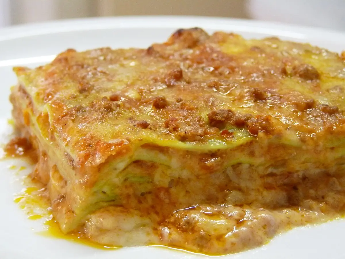 A square of lasagne with thin green pasta layers, ragù and béchamel on a white plate