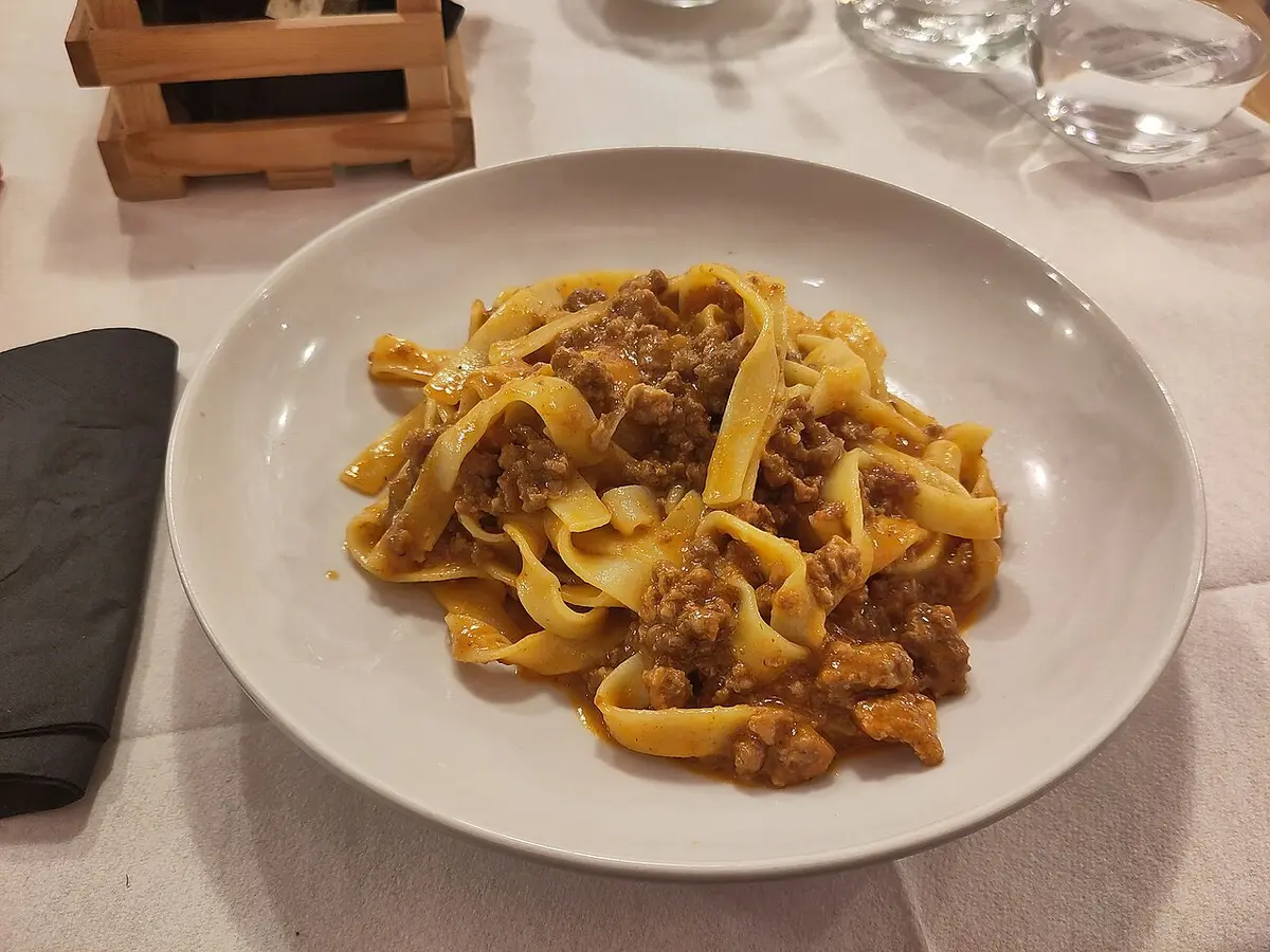 Tagliatelle al ragù in a white bowl on a trattoria table