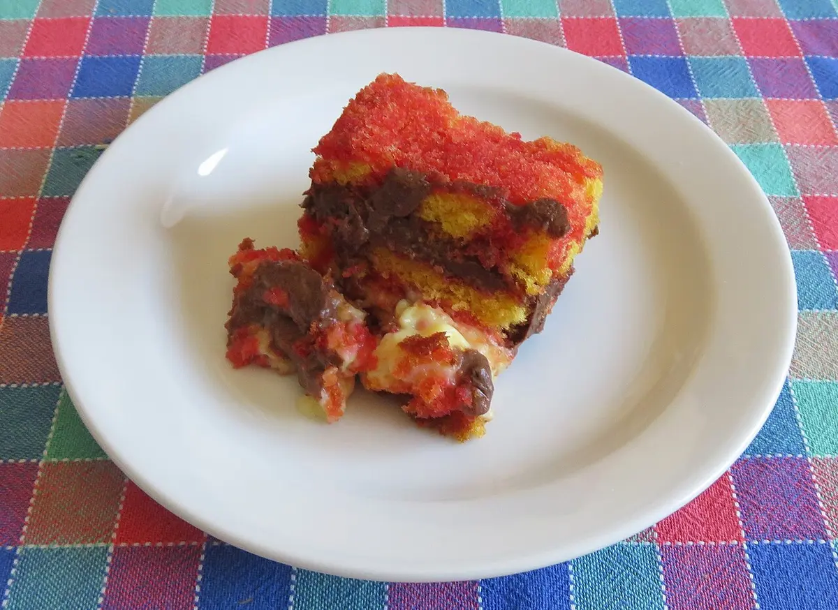 A portion of zuppa inglese on a white plate, red-soaked sponge layered with custard and chocolate