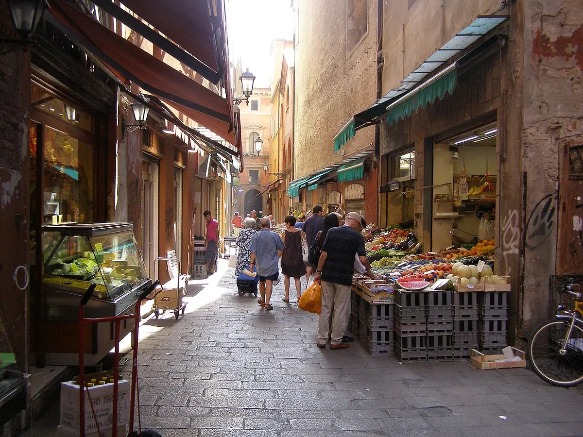 A narrow market lane in the Quadrilatero with fruit and vegetable stalls under awnings