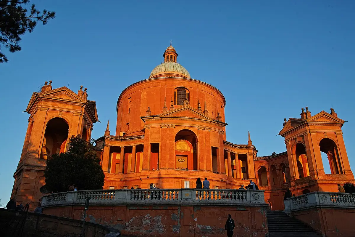 The sanctuary of the Madonna di San Luca glowing orange at sunset under a clear sky, its curved porticoes on each side