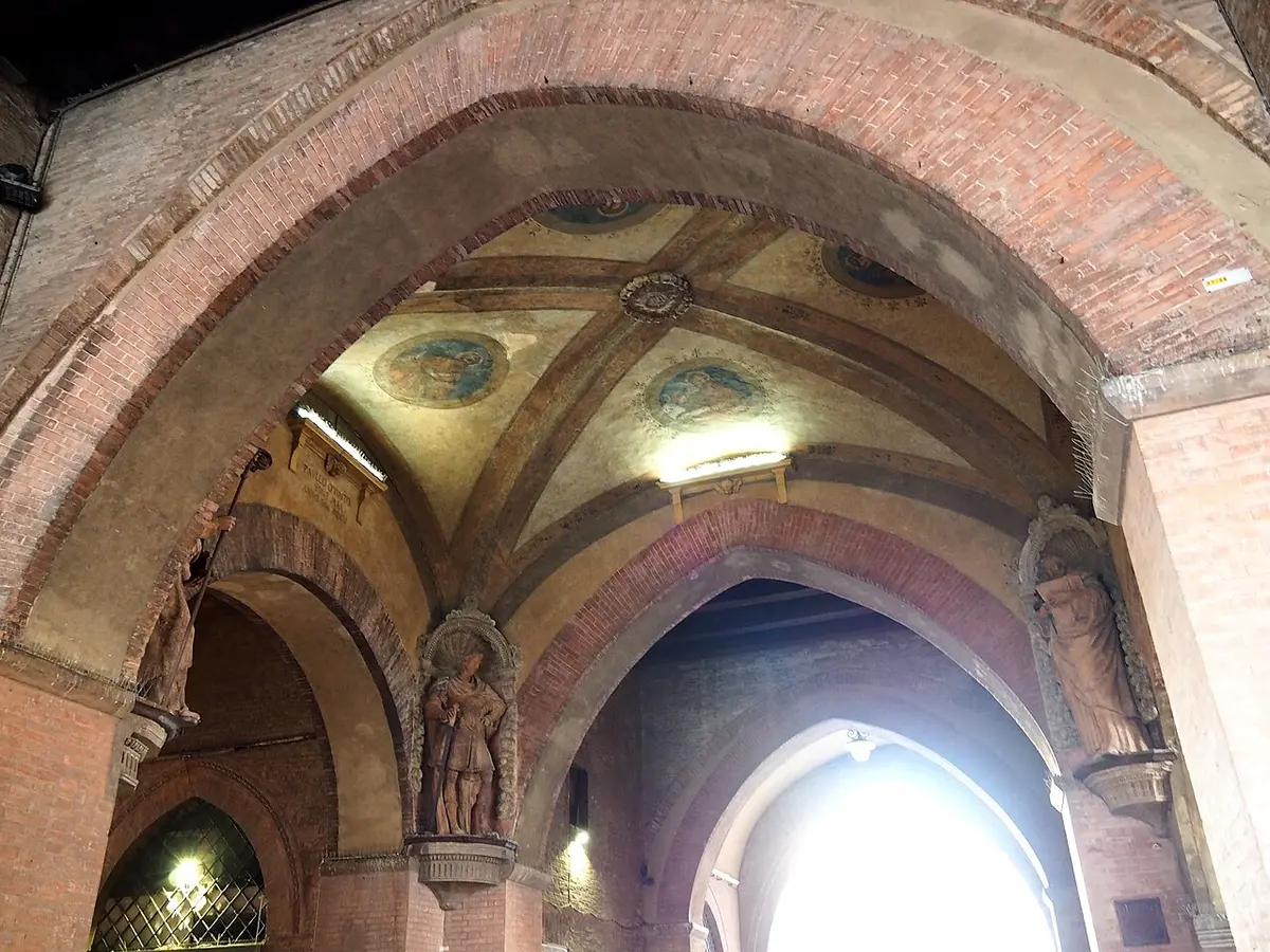 The brick vaults of the Voltone del Podestà, painted with roundels, with a terracotta saint in a corner niche