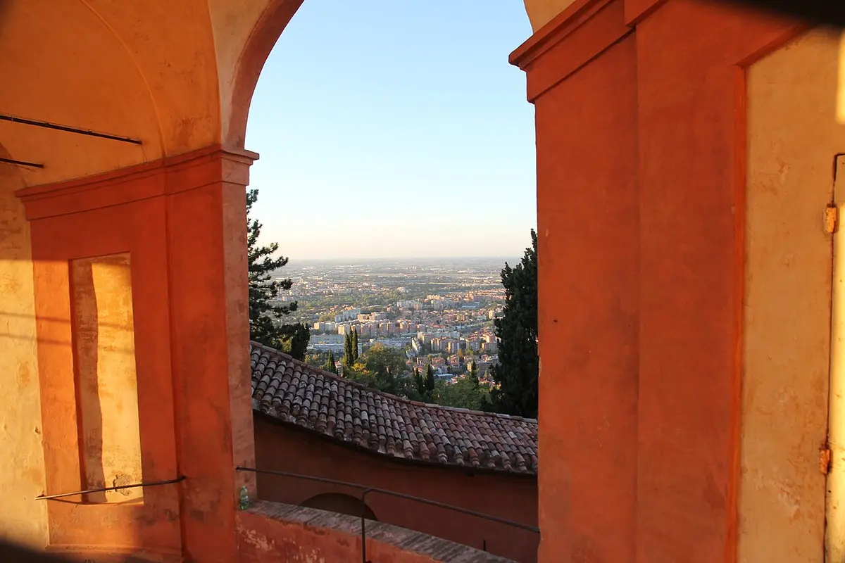 Bologna and the plain seen through an arch of the portico, over a tiled roof