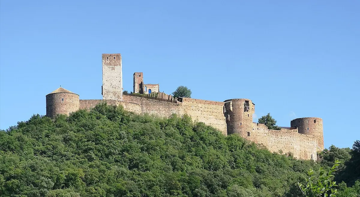 The long walls and round towers of Sigmundskron Castle on a wooded hill