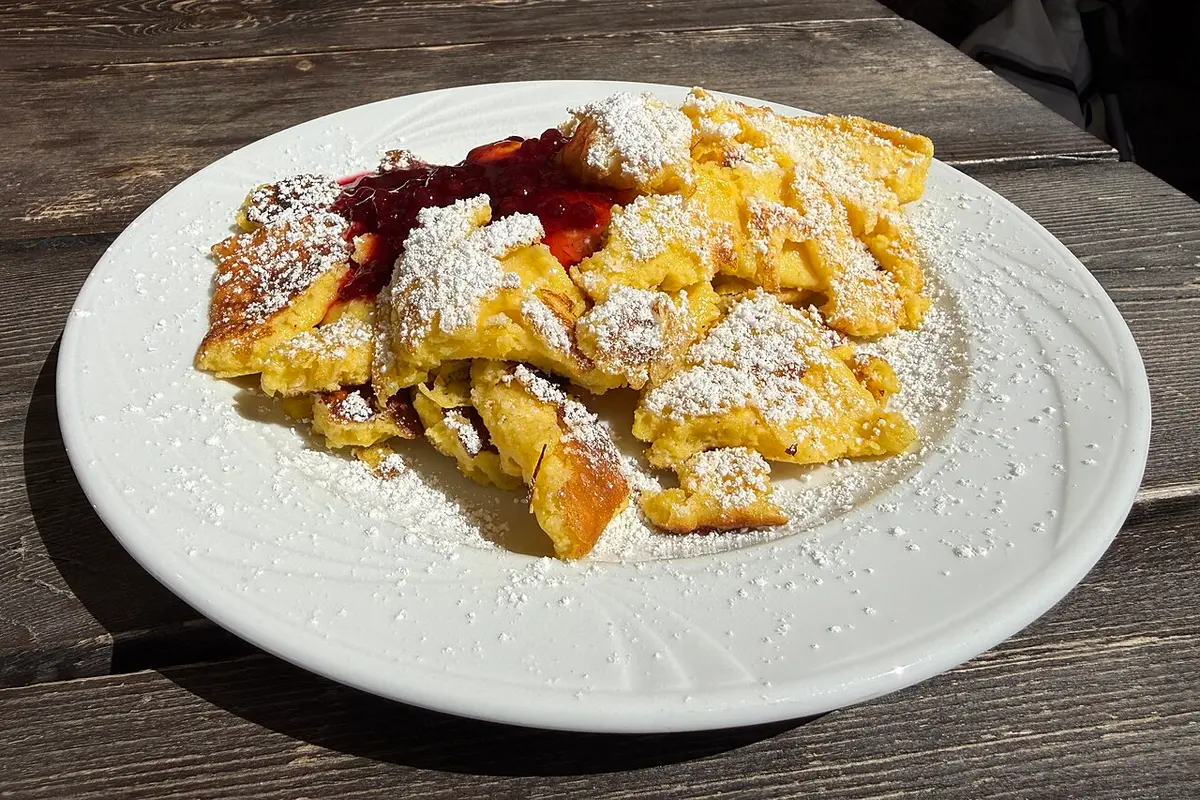 Kaiserschmarrn, torn pieces of pancake dusted with powdered sugar, with red berry jam on a white plate