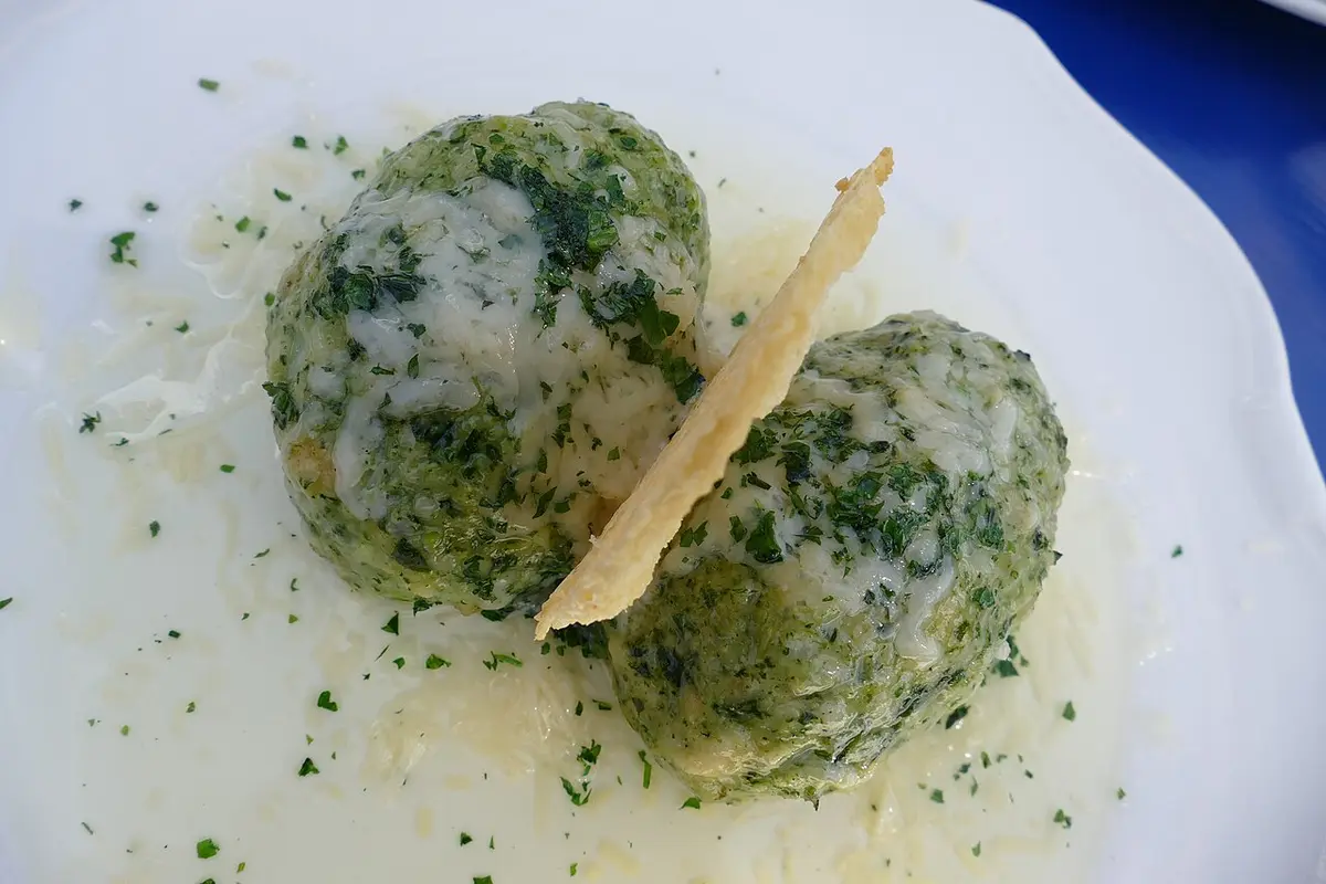 Two spinach Knödel with melted butter and grated Parmesan on a white plate
