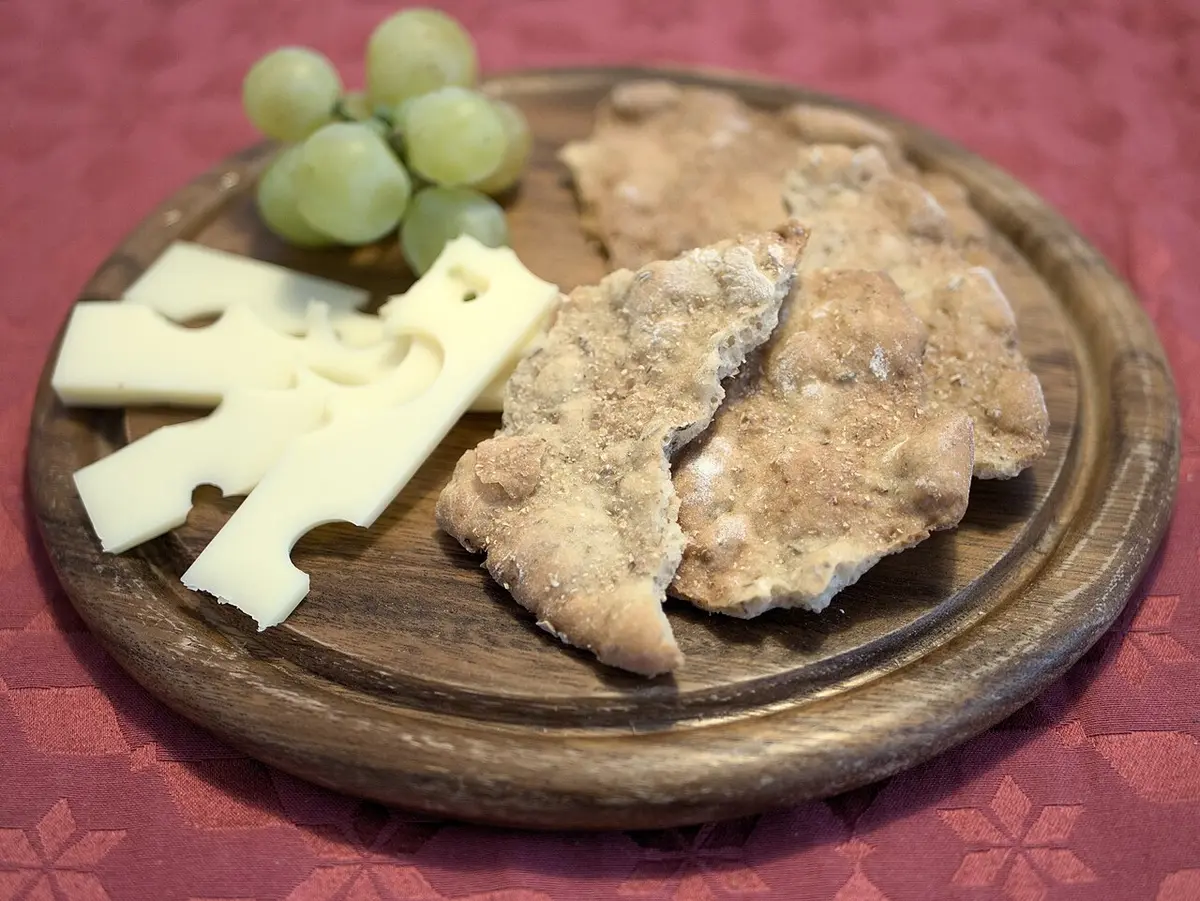Pieces of Schüttelbrot, a crisp rye flatbread, on a wooden board with sliced cheese and green grapes