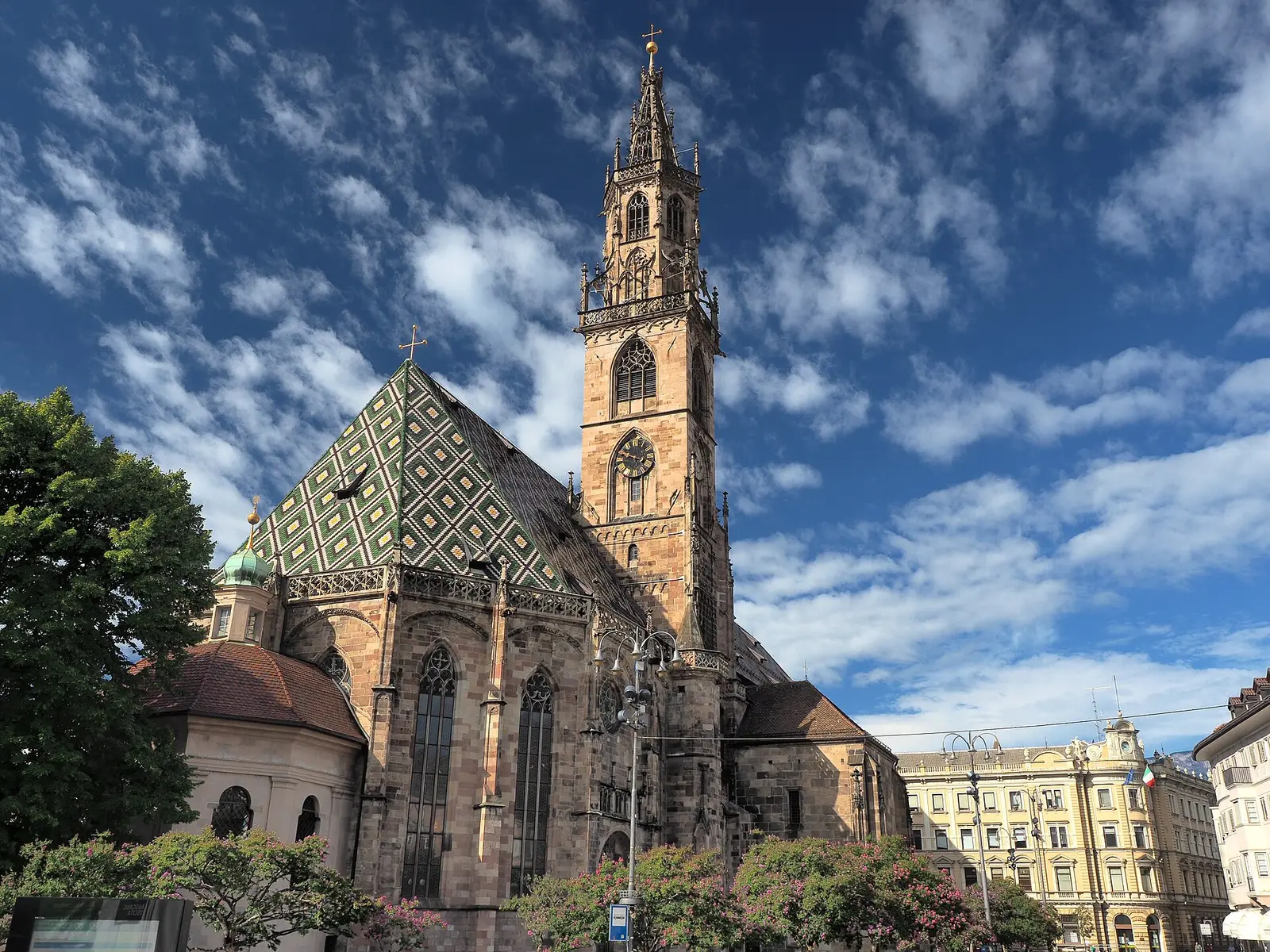 Bolzano Cathedral, its roof of green and yellow glazed tiles and its Gothic bell tower against a blue sky