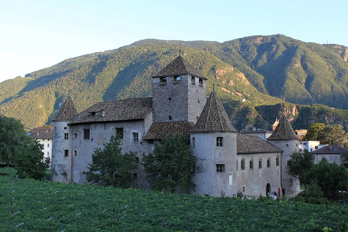 Castel Mareccio with its round corner towers among vineyards, a mountain behind