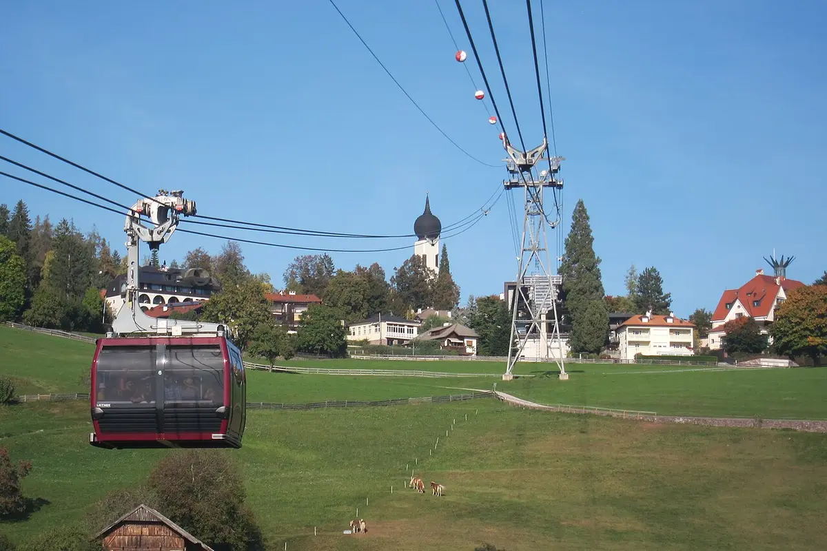 A red cable car cabin arriving over meadows at Oberbozen, above Bolzano, a church tower behind