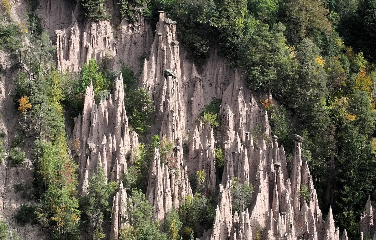 Pale columns of eroded clay, some topped by boulders, rising from a wooded ravine