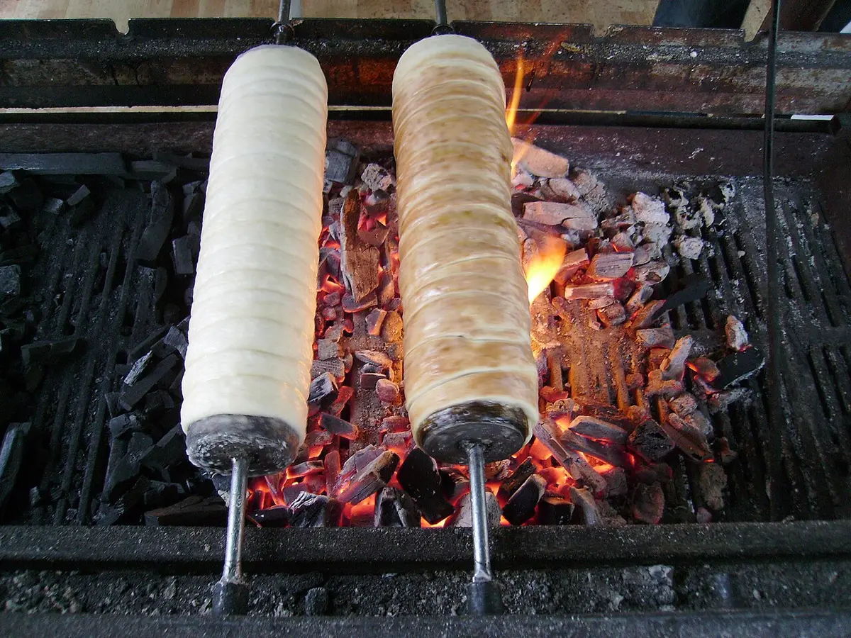 Two chimney cakes roasting on spits over glowing charcoal
