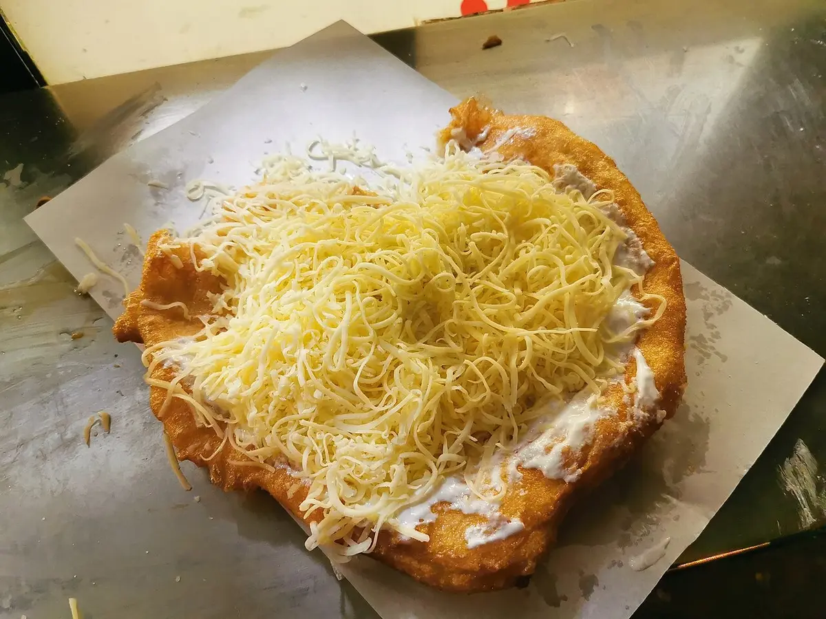A lángos spread with sour cream and grated cheese, served on paper