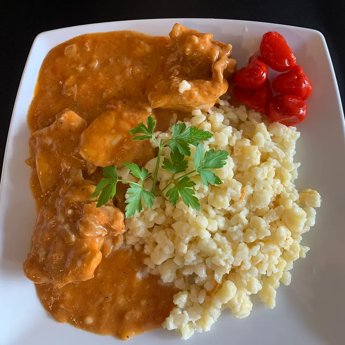 Chicken in a creamy paprika sauce beside nokedli dumplings