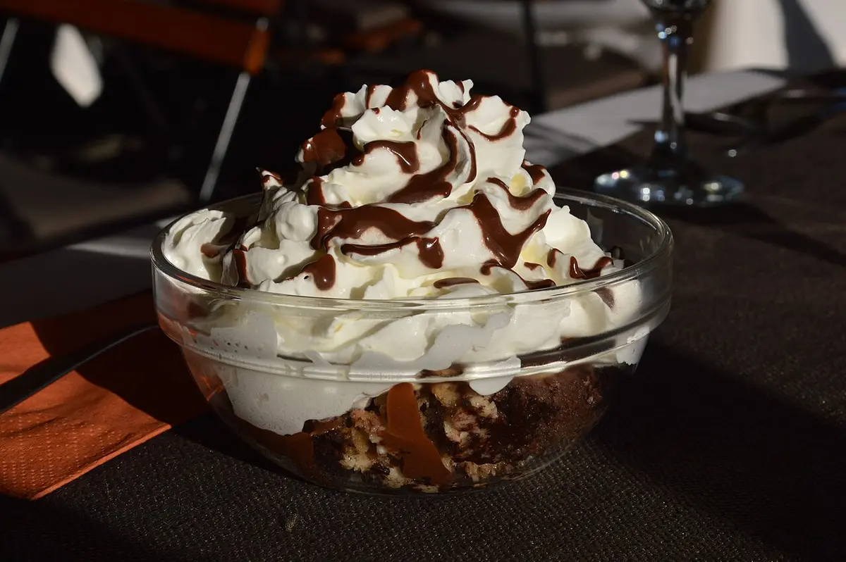 Somlói galuska in a glass bowl, topped with whipped cream and chocolate sauce