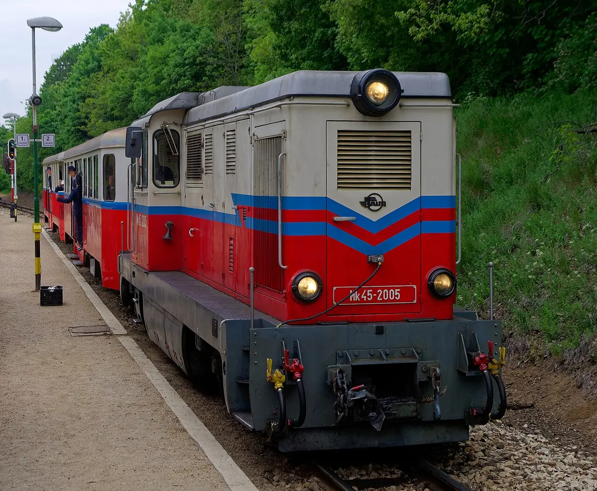 A red and cream diesel train of the Children’s Railway at a station in the Buda Hills woods