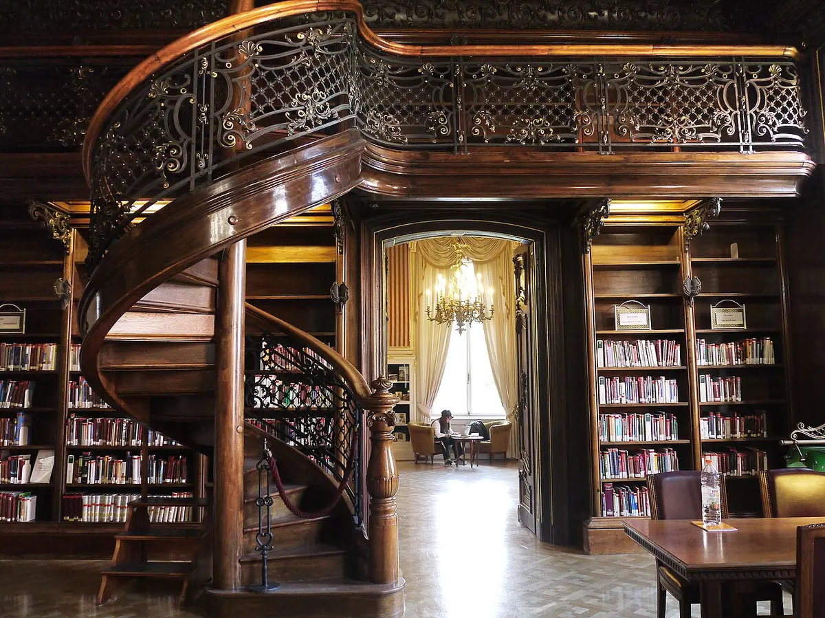 A carved wooden spiral staircase in a paneled reading room of the Szabó Ervin Library