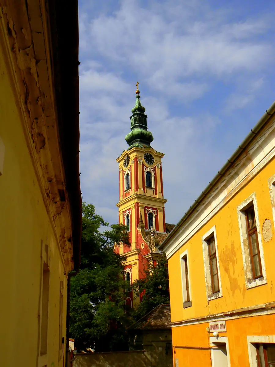 The red and yellow baroque tower of the Belgrade Cathedral in Szentendre against a blue sky