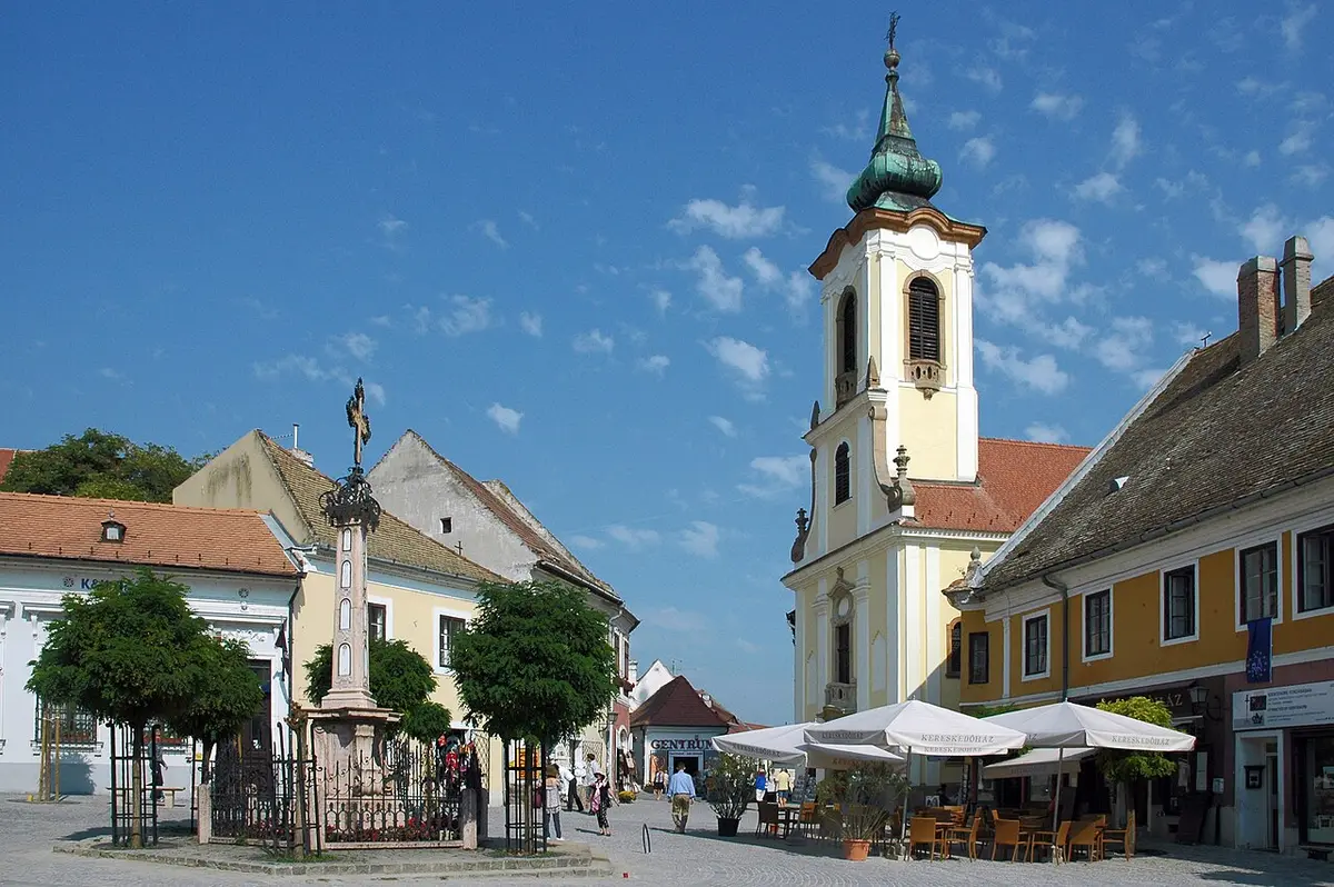 Szentendre’s main square with an iron cross on a stone pillar and a church tower behind