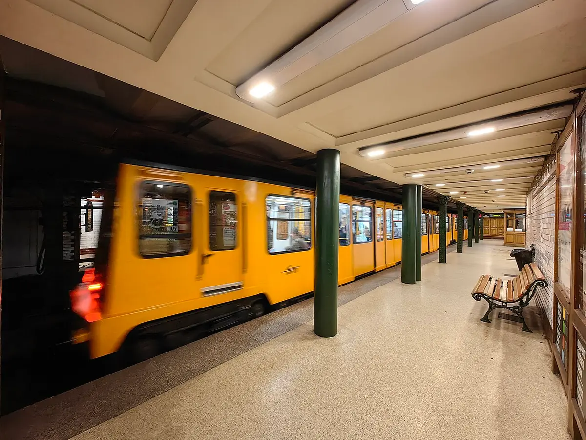 A small yellow train of the M1 line in Kodály körönd station, with green iron columns and tiled walls
