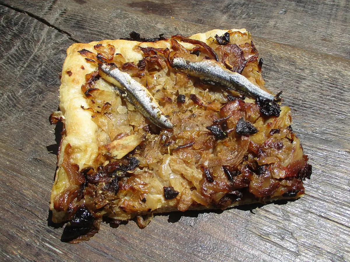 A slice of pissaladière topped with soft brown onions, anchovies and black olives