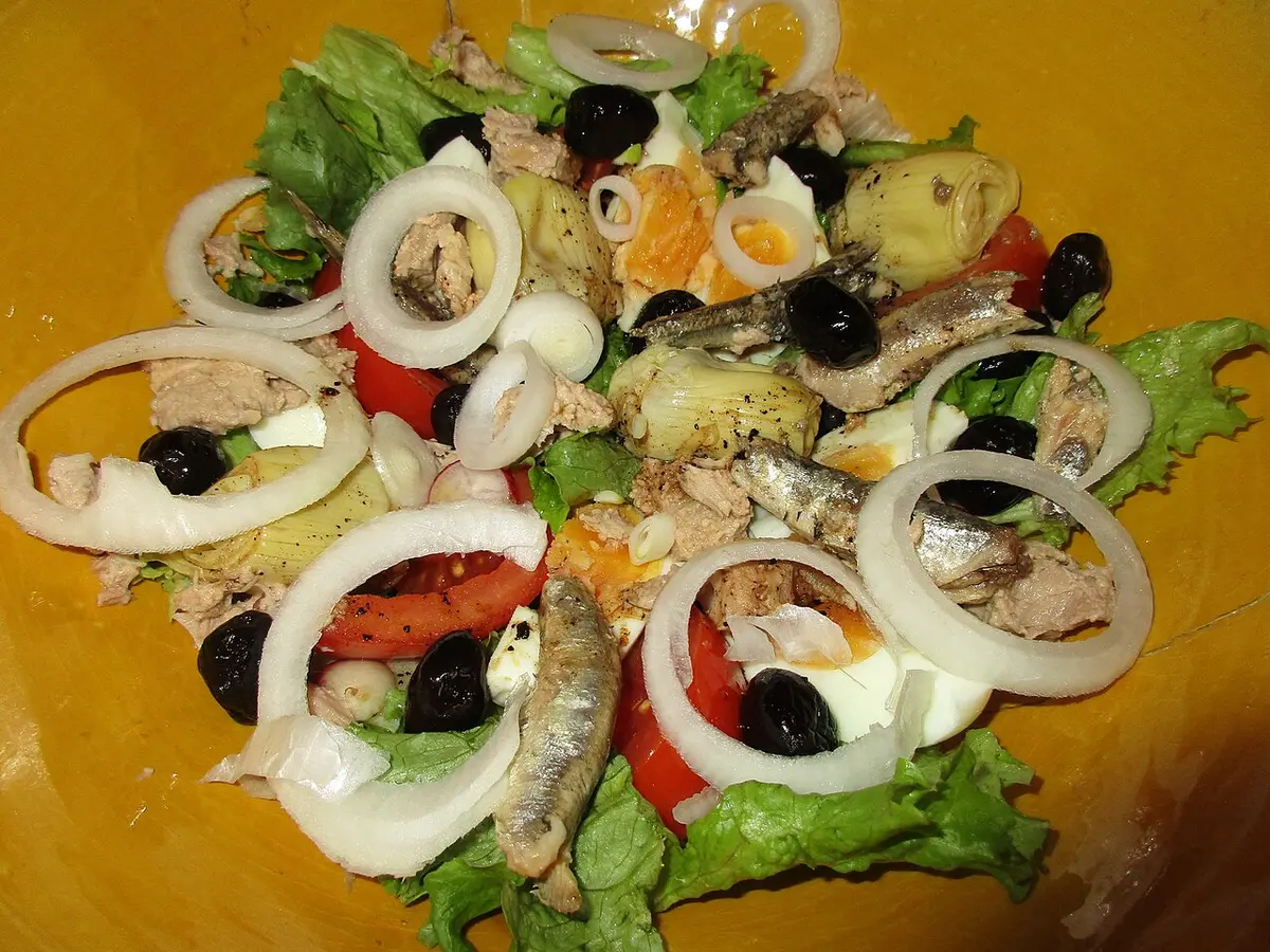 A salade niçoise with anchovies, black olives, onion rings, tomato and lettuce