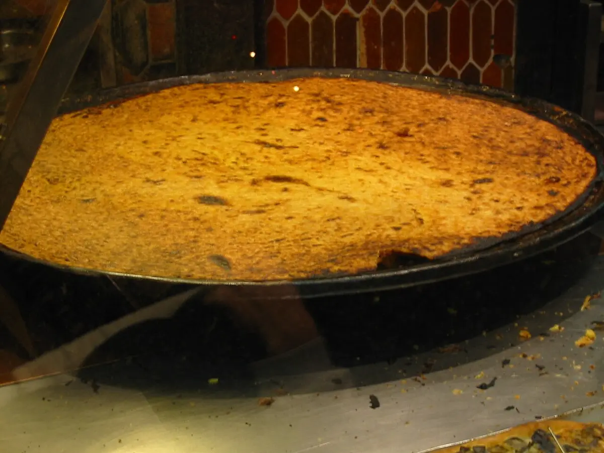 A large, thin chickpea pancake with a crisp golden top in a wide round pan