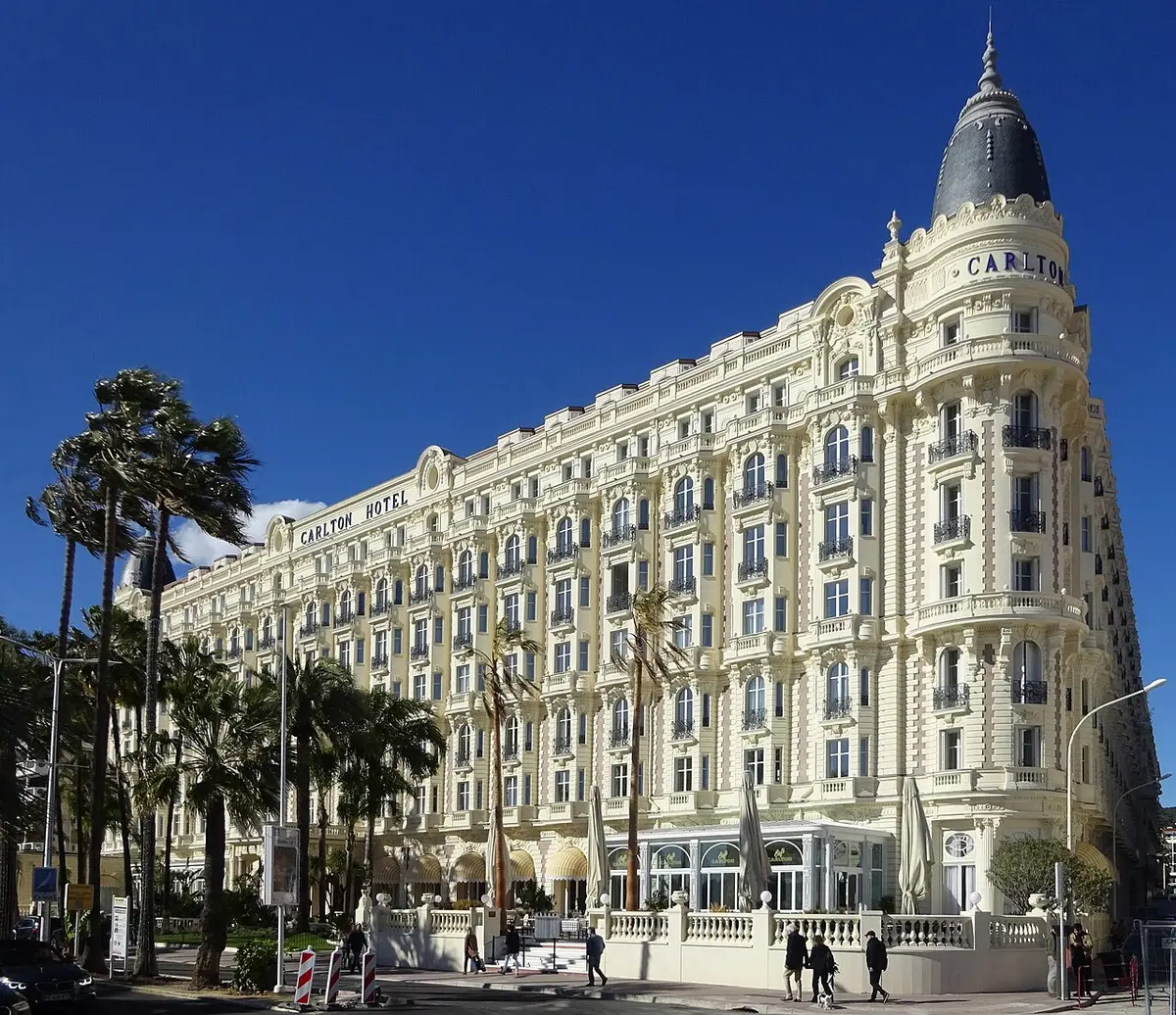 The white Belle Époque front of the Carlton hotel with its domed corner towers, behind palm trees