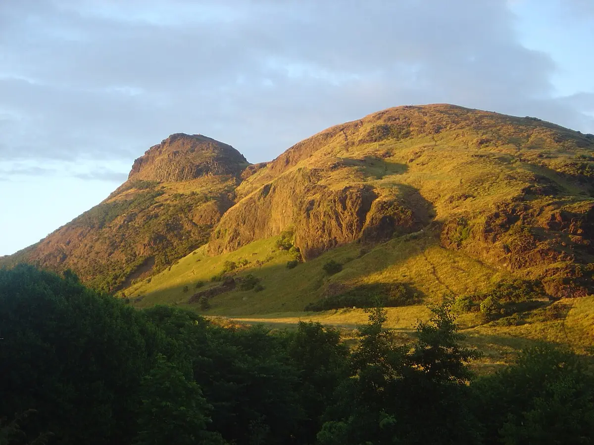 Arthur’s Seat and the crags of Holyrood Park lit gold by low sun, above a line of trees