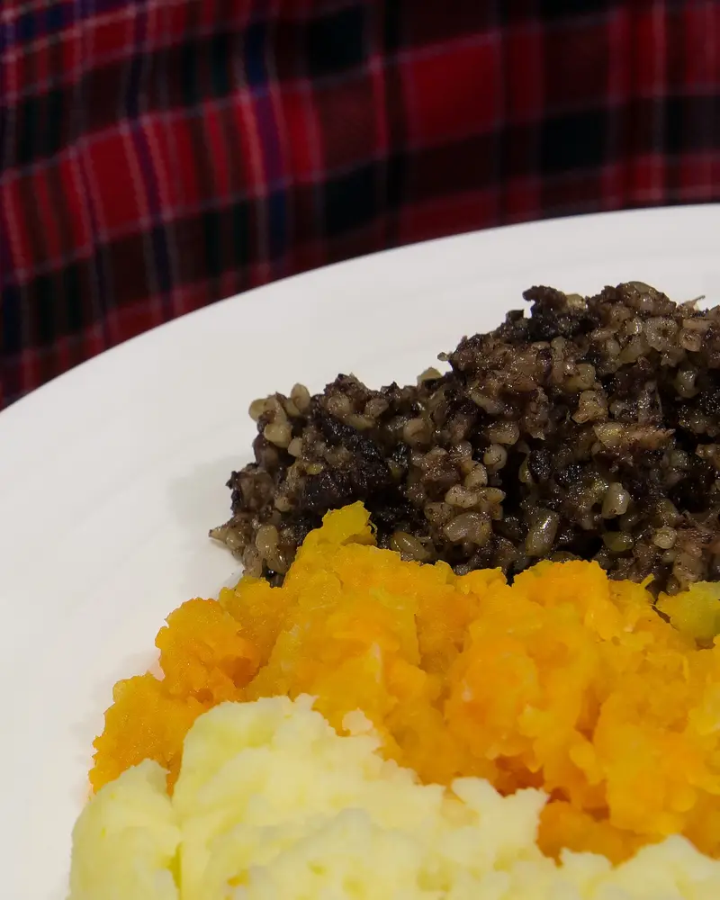 Haggis with mashed swede on a white plate over a tartan cloth