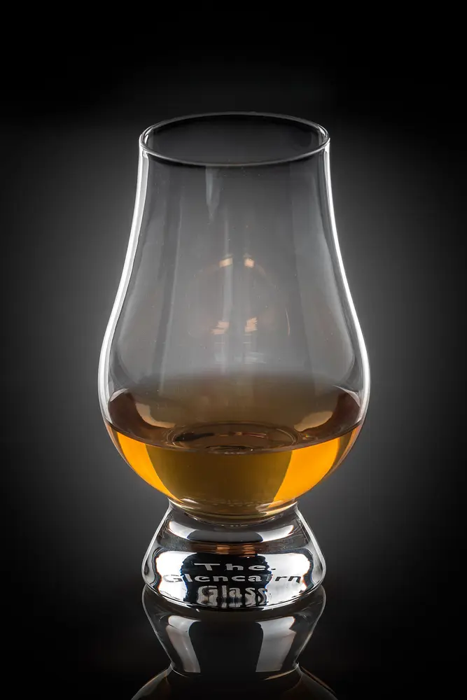 A dram of amber whisky in a tulip-shaped Glencairn glass against a dark background