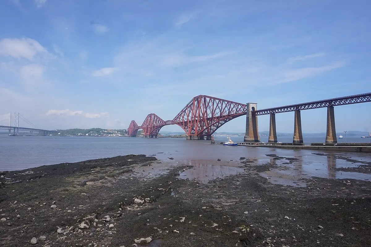 The red steel cantilevers of the Forth Bridge crossing the Firth of Forth, seen from the shore at South Queensferry