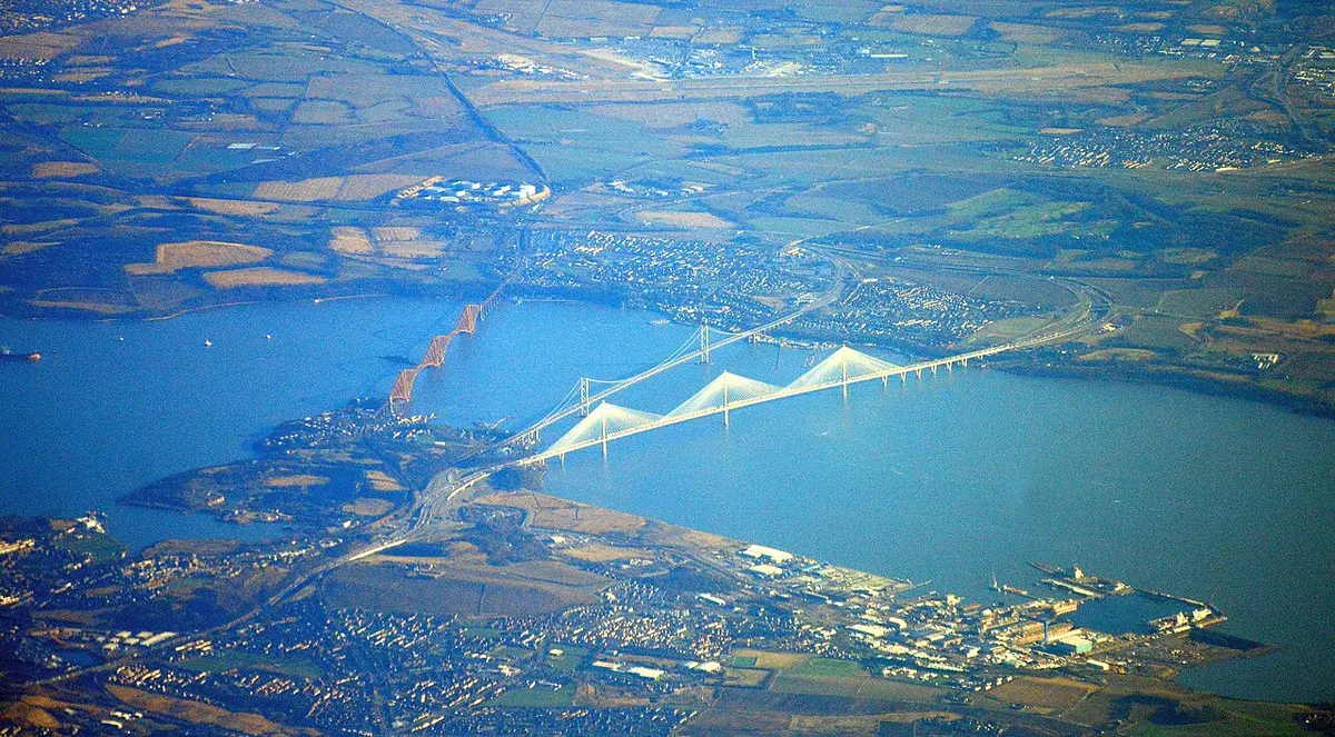 Aerial view of the three Forth bridges side by side across the firth: the red rail bridge, the suspension road bridge and the white cable-stayed Queensferry Crossing